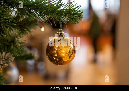 Un sapin de Noël doré est délicatement suspendu d'une branche de pin festive, éclairé par la lumière chaude d'une fenêtre voisine Banque D'Images