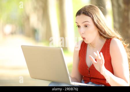 Une femme surprise qui vérifie le contenu d'un ordinateur portable, seule dans un parc Banque D'Images