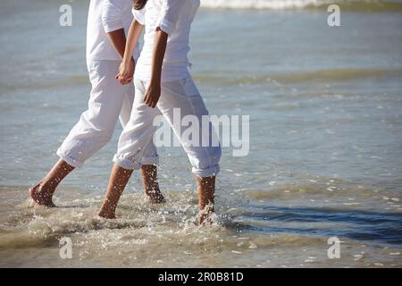 Calme dans les eaux fraîches. un couple méconnaissable marchant le long d'une plage avec son pantalon enroulé. Banque D'Images