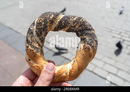 Main tenant obwarzanek krakowski bretzel sur le marché de la place principale de Cracovie, avec oiseau de pigeon attendant des miettes de nourriture. Nourrir des pigeons à Cracovie, en Pologne. Banque D'Images