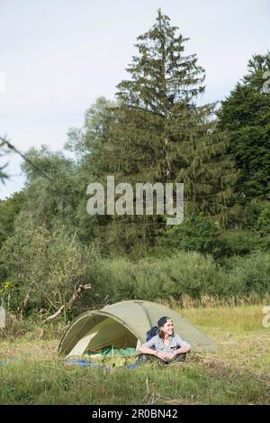 Adolescent assis près de sa tente de camp dans la forêt, Bavière, Allemagne Banque D'Images