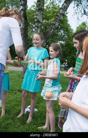 Femme entraîneur distribuant des oeufs aux enfants pour la course de cuillère dans un parc, Munich, Bavière, Allemagne Banque D'Images