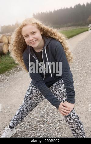 Portrait d'une adolescente qui s'étire les jambes sur le sentier et souriant à l'aube, Bavière, Allemagne Banque D'Images