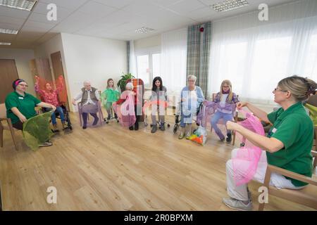 Les filles avec des infirmières et une femme âgée faisant de l'exercice sportif doux avec le tissu dans la maison de repos Banque D'Images