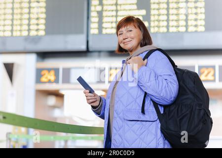 Femme adulte voyageant avec des bagages à main, sac à dos tient le passeport et attend le voyage de vol à l'aéroport international terminal. Femme d'âge moyen Go Banque D'Images