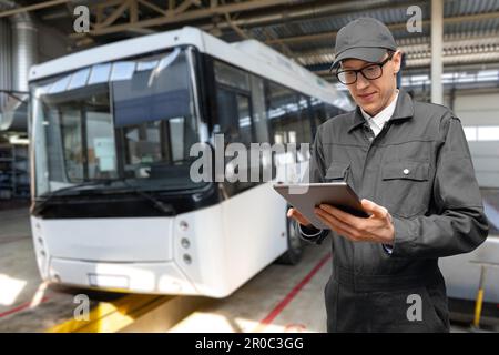 Chef de service avec tablette numérique sur l'arrière-plan du bus dans le garage. Photo de haute qualité Banque D'Images