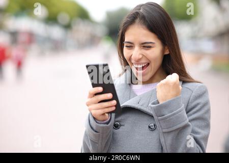 Une femme excitée vérifie le contenu du téléphone dans la rue Banque D'Images