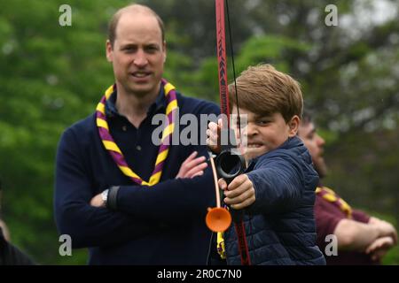 Le Prince George, observé par le Prince de Galles, tente de tir à l'arc tout en se joignant à des bénévoles pour aider à rénover et à améliorer le 3rd Upton Scouts Hut à Slough, dans le cadre de la grande aide, pour marquer le couronnement du roi Charles III et de la reine Camilla. Date de la photo: Lundi 8 mai 2023. Banque D'Images