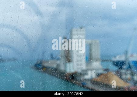 bâtiments sur un quai portuaire flou vus d'un bateau de croisière à travers une fenêtre vitrée recouverte de gouttes de pluie Banque D'Images