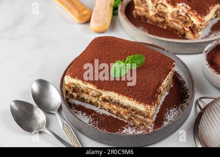 Dessert italien traditionnel tiramisu sur des assiettes. Portions de gâteau au tiramisu maison avec menthe fraîche et cuillères Banque D'Images