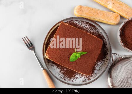 Tiramisu de dessert italien traditionnel sur l'assiette avec une tasse de café et une fourchette. Portion de gâteau au tiramisu maison à la menthe fraîche Banque D'Images