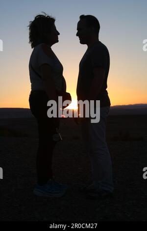 Silhouette d'un couple face à l'autre au coucher du soleil Banque D'Images