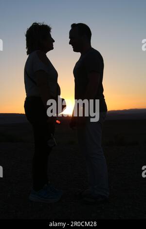 Silhouette d'un couple face à l'autre au coucher du soleil Banque D'Images