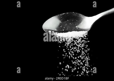 Macro photographie d'une cuillère à café avec le sucre blanc en fricleur sur un fond noir, espace de copie. Banque D'Images