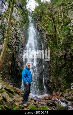 Tourist attraction of Germany - falls of Burgbach Waterfall near Schapbach, Black Forest, Baden-Wurttemberg, Germany. Man hiker in blue jacket Banque D'Images
