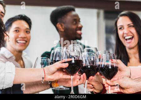 Des amis multiraciaux qui toasent du vin rouge au restaurant. Groupe de jeunes qui s'amusent à table de winebar intérieure. Dîner style de vie et amitié Banque D'Images