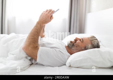 Vue latérale Happy man utilisant le téléphone dans le lit à la maison Banque D'Images