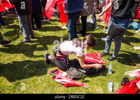 Izmir,Konak,Turquie 04.30.2023 Une fille aux cheveux noirs prend de l'eau et son drapeau turc dans son sac à main, courbée sur de l'herbe verte dans une foule de gens Banque D'Images