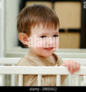 Portrait d'un bébé heureux près des barres du berceau. Un enfant souriant semble se tenir sur la main courante du lit. Enfant âgé d'environ deux ans (un an et Banque D'Images