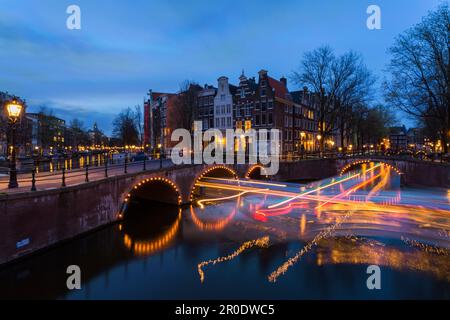 Ponts illuminés à l'heure bleue du crépuscule à Amsterdam, Hollande, pays-Bas en avril exposition longue exposition multiple avec des lumières de bateaux passant sous le pont Banque D'Images