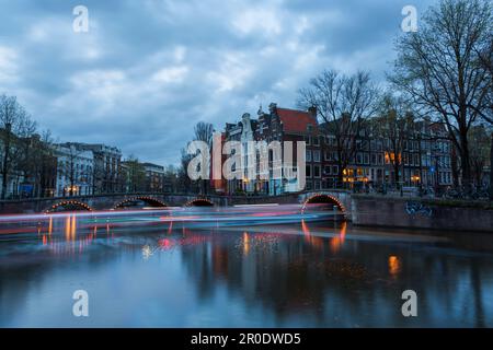 Ponts illuminés à l'heure bleue du crépuscule à Amsterdam, Hollande, pays-Bas en avril exposition longue exposition multiple avec des lumières de bateaux passant sous le pont Banque D'Images