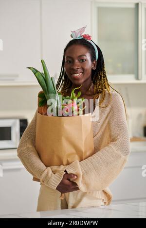 Portrait d'une femme noire heureuse debout dans la cuisine avec sac en papier d'épicerie fraîche Banque D'Images