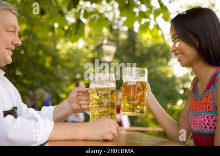 Un homme bavarois plus âgé et une femme asiatique se toasting, Munich, Bavière Banque D'Images