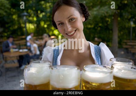 Jeune serveuse avec des bières steins dans le café en plein air, Munich, Bavière Banque D'Images