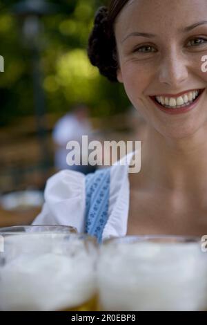 Jeune serveuse avec des bières steins dans le café en plein air, Munich, Bavière Banque D'Images