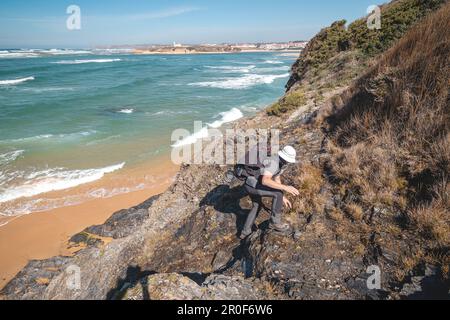 Homme âgé essayant de gravir un rocher au sommet d'une montagne par une journée ensoleillée dans la région d'Odemira, à l'ouest du Portugal. Flâner le long du Fisherman Trai Banque D'Images