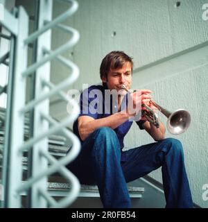 Homme jouant une trompette, assis sur les escaliers, Allemagne Banque D'Images