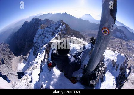 Homme relaxant au pied de la croix du sommet, Zugspitze, Bavière, Allemagne Banque D'Images