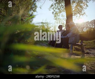 Pensionnés assis sur un banc sur les berges de l'auberge profitant du soleil du soir, près de Bad Füssing, Bavière, Allemagne Banque D'Images