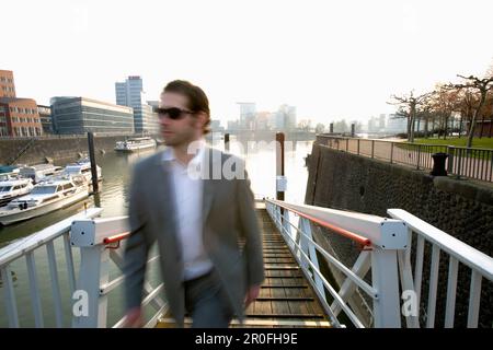 Homme d'affaires traversant Media Harbour, Düsseldorf, capitale de l'État de NRW, Rhénanie-du-Nord-Westphalie, Allemagne Banque D'Images