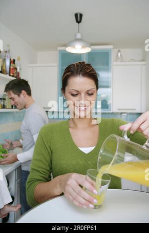 Jeune femme versant un verre de jus, homme en arrière-plan, Munich, Allemagne Banque D'Images