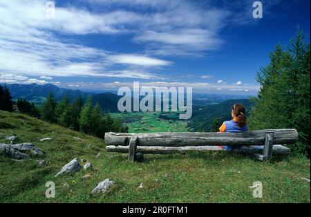 Femme assise sur un banc avec vue sur la vallée avec Inzell, cabane alpine Kohleralm, Alpes de Chiemgau, Chiemgau, Bavière, Allemagne Banque D'Images