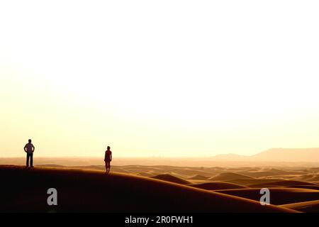 Silhouette de couple dans le désert regarder le coucher du soleil, Dubaï, Émirats arabes Unis, Émirats Arabes Unis Banque D'Images
