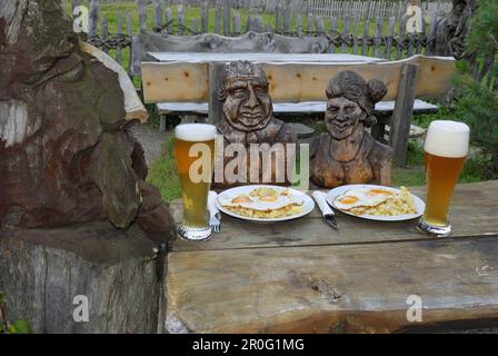 Couple sculpté à une table avec de la nourriture et de la bière de blé, chalet alpin Sulzenau, Alpes de Stubaier, Stubai, Tyrol, Autriche Banque D'Images