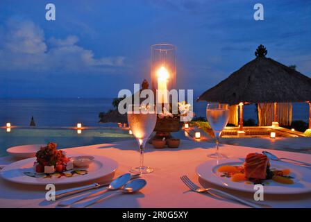 Une table est posée à la piscine de l'Amankila Resort dans la soirée, Candi Dasa, l'est de Bali, l'Indonésie, l'Asie Banque D'Images