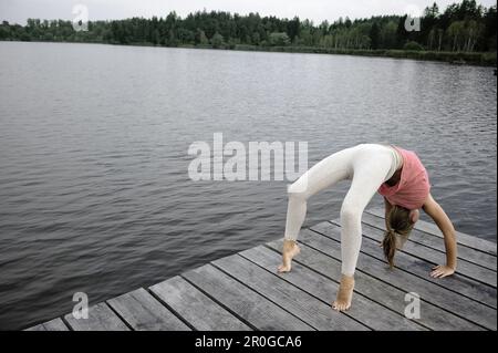 Jeune femme qui fait un pont sur une jetée au lac Starnberg, Bavière, Allemagne Banque D'Images