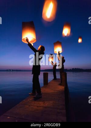 Trois personnes tenant des lanternes Sky, lac Chiemsee, Bavière, Allemagne Banque D'Images