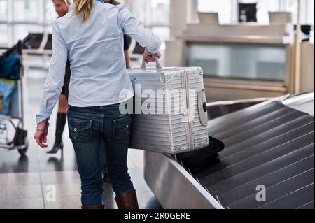 Femme prenant une valise à l'extérieur d'une courroie transporteuse de bagages, à l'aéroport de Munich, en Bavière, en Allemagne Banque D'Images