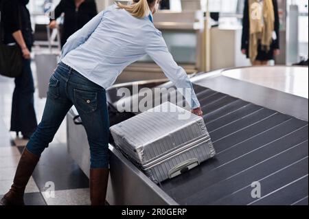 Femme prenant une valise à l'extérieur d'une courroie transporteuse de bagages, à l'aéroport de Munich, en Bavière, en Allemagne Banque D'Images