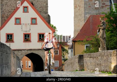 Cycliste femelle passant le pont, porte de ville en arrière-plan, Ornbau, sentier de cycle Altmuehltal, Bavière, Allemagne Banque D'Images
