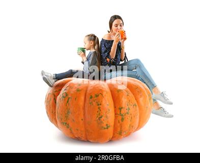 Femme et sa petite fille avec une savoureuse boisson au cacao assis sur une grande citrouille sur fond blanc Banque D'Images