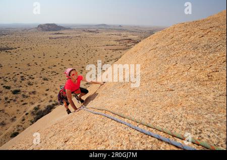Woman climbing au red rock visage sur Savannah, Grand Spitzkoppe, Namibie Banque D'Images