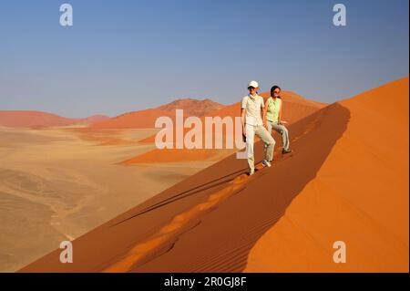 Deux femmes se tenant sur une dune de sable rouge à Sossusvlei, dune 45, Sossusvlei, parc national Namib Naukluft, désert Namib, Namib, Namibie Banque D'Images