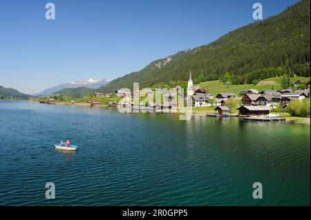 Deux personnes d'un bateau d'aviron sur le lac Weissensee, village Gatschach en arrière-plan, le lac Weissensee, Carinthie, Autriche, Europe Banque D'Images