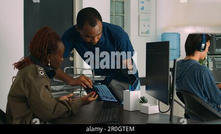 Équipe de programmeurs analysant les algorithmes de codage sur ordinateur portable et ordinateur dans bureau d'agence numérique. Les développeurs système discutent du script de base de données et du serveur de pare-feu, de l'interface Big Data. Banque D'Images