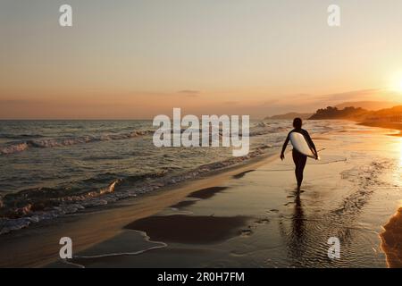 Surfer marcher le long de la plage au coucher du soleil, Castiglione della Pescaia, Mer Méditerranée, province de Grosseto, Toscane, Italie, Europe Banque D'Images